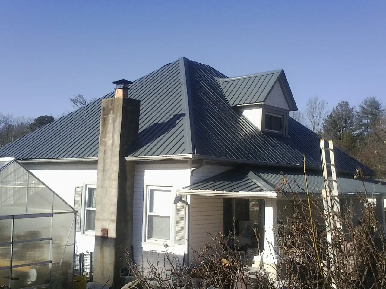 Dark blue standing seam metal roof on a white farmhouse with dormer — Slate & Tile Roof Repair by Roofing Brothers in Neal