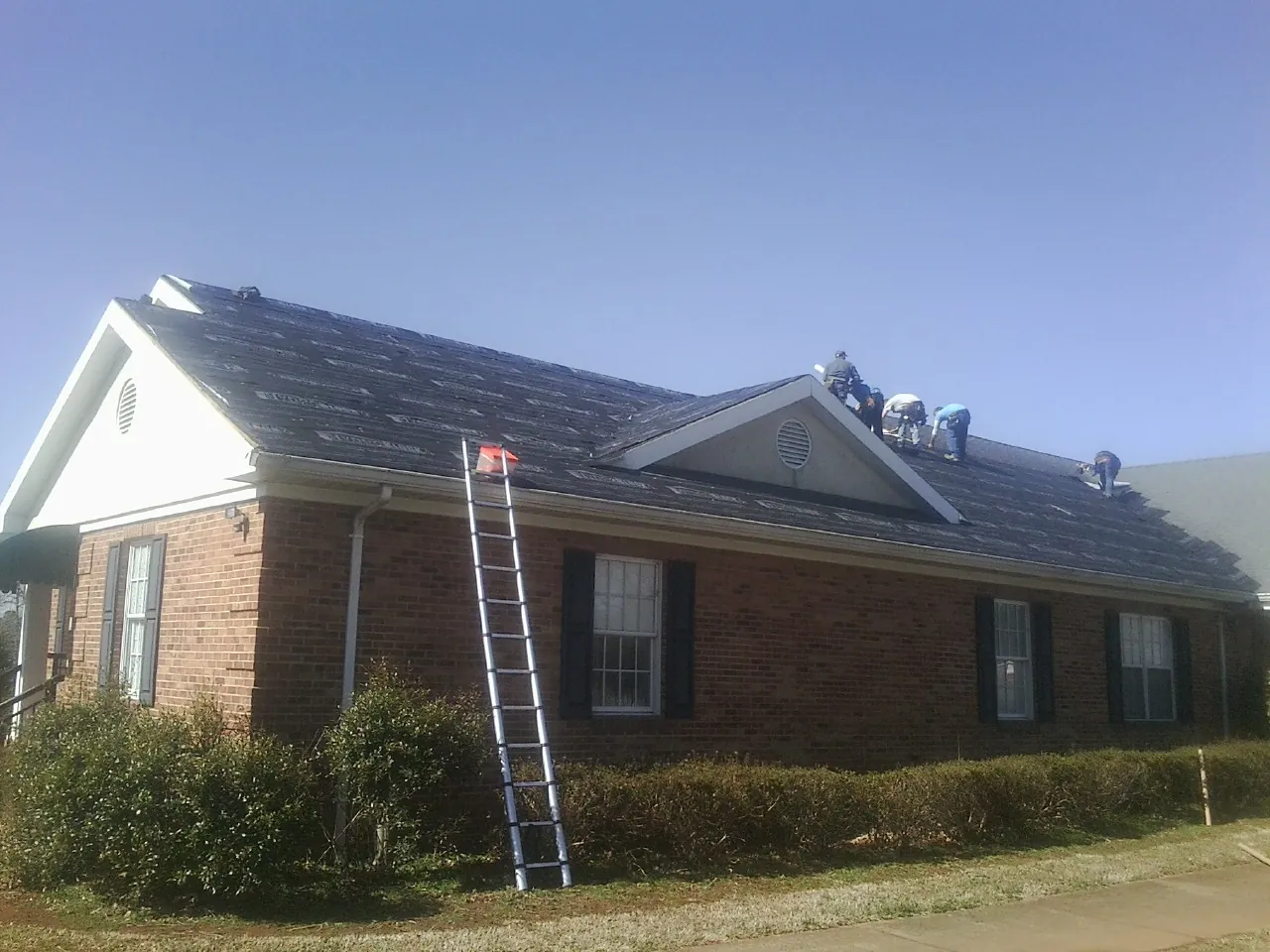 Crew tearing shingles off a brick ranch roof with a ladder set — Emergency Roof Repair work by our crew in Neal