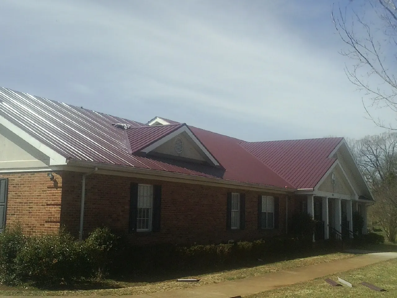 Red metal roof with gabled entries on a long brick building, from a Hail Damage Roof Repair job in Neal