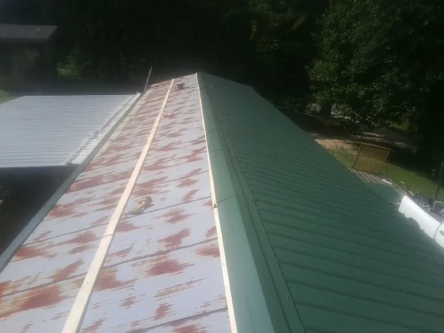 Old rusted panels beside newly installed green metal roofing — Wind Damage Roof Repair by Roofing Brothers in Neal