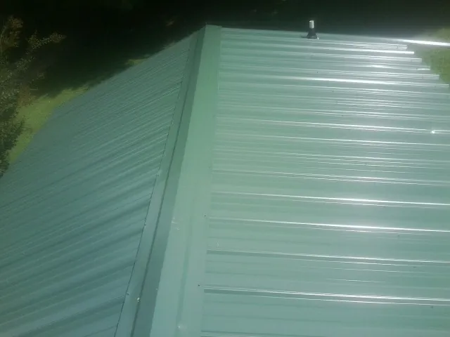 New green metal panels meeting at the ridge of a roof — Flat Roof Repair work by our crew in Neal