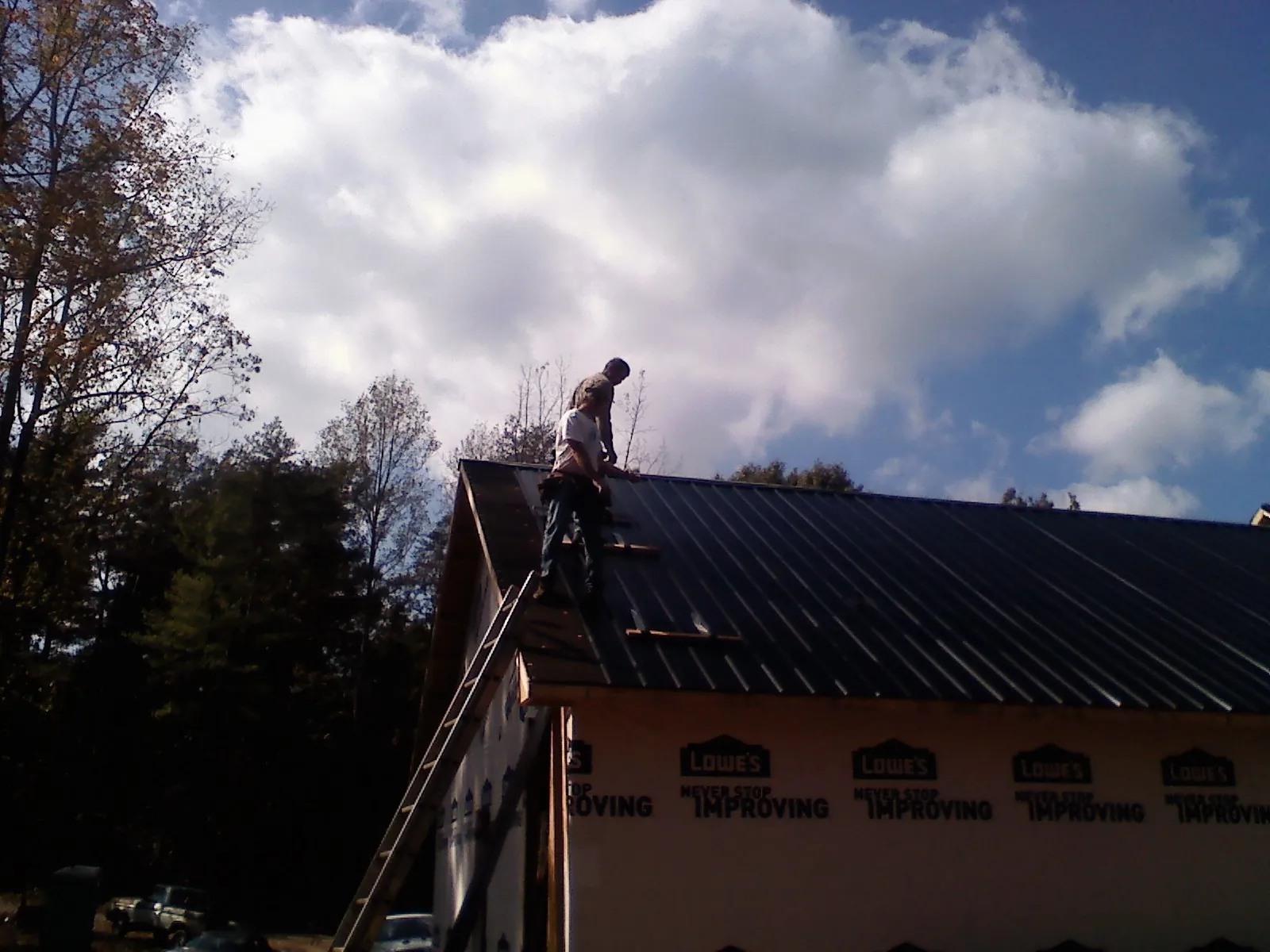 Roofer fastening dark metal panels high against a cloudy sky, from a Roof Inspection job in Neal