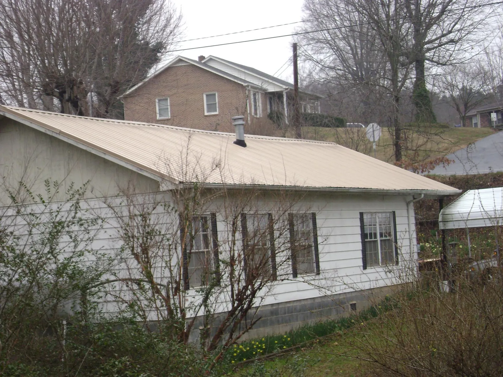 Tan metal roof on a white sided house set into a hillside — Commercial Roofing by Roofing Brothers in Neal