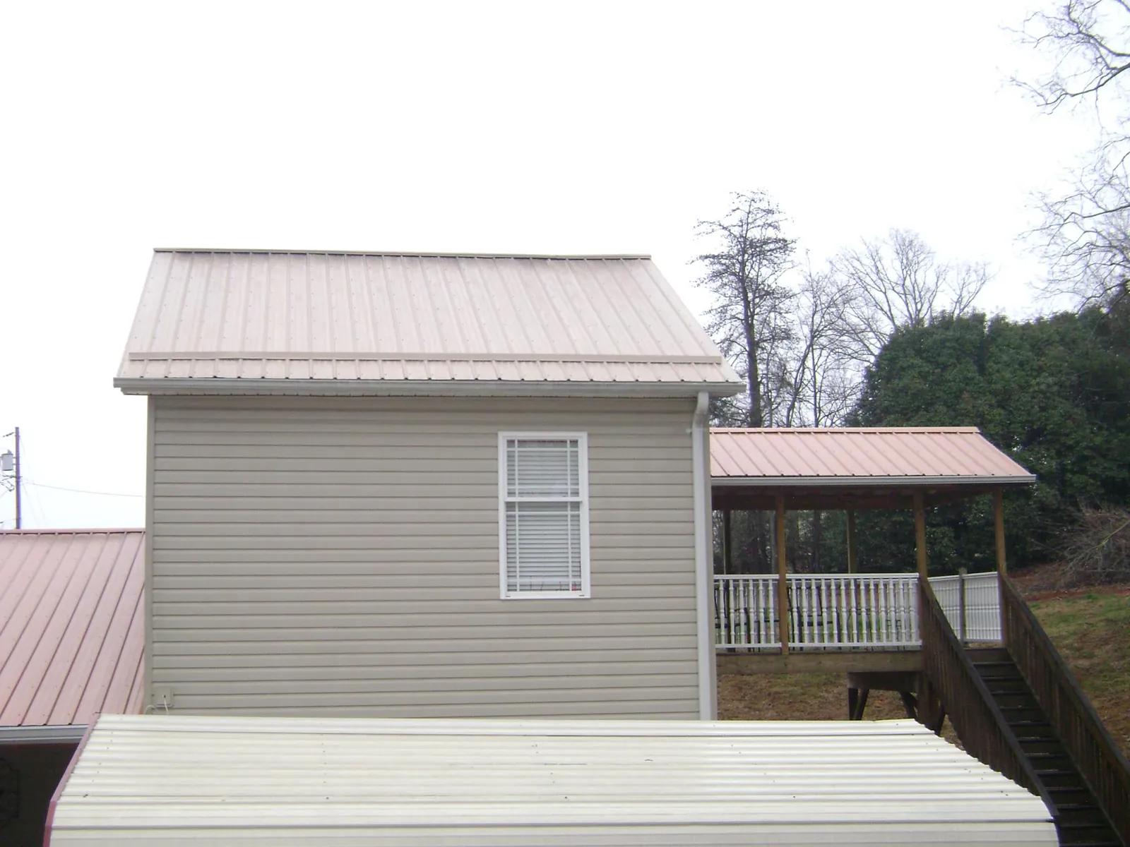 Tan metal roofs on a two story addition and attached porch, from a Roof Replacement job in Neal